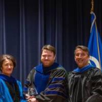 Provost Mili takes picture with 2 men on stage